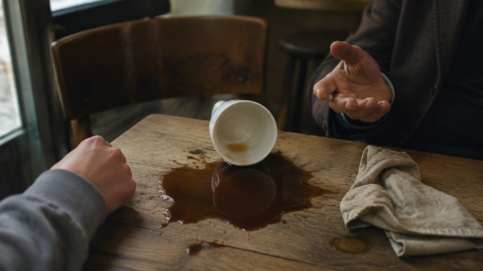 Une tasse en porcelaine renversée laisse le café se répandre sur une table claire